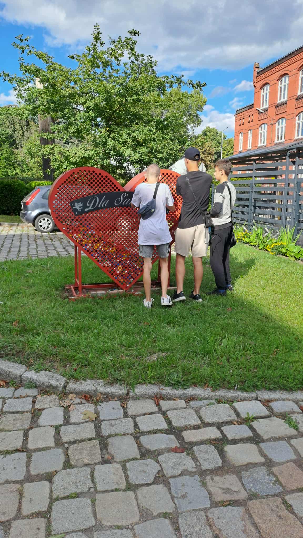 Na obrazku widać: grupę osób, trawę , czerwone serce