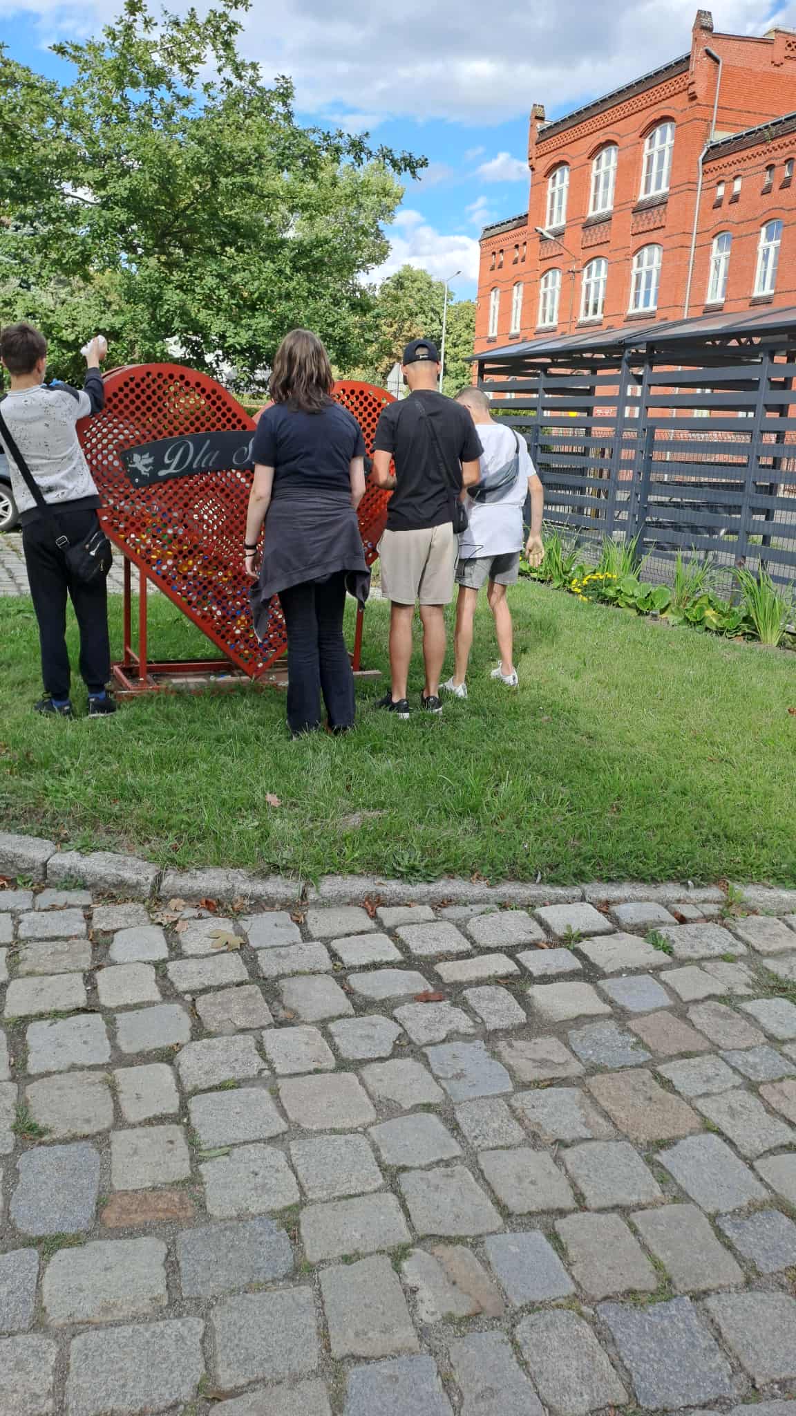Na obrazku widać: grupę osób, trawę , czerwone serce