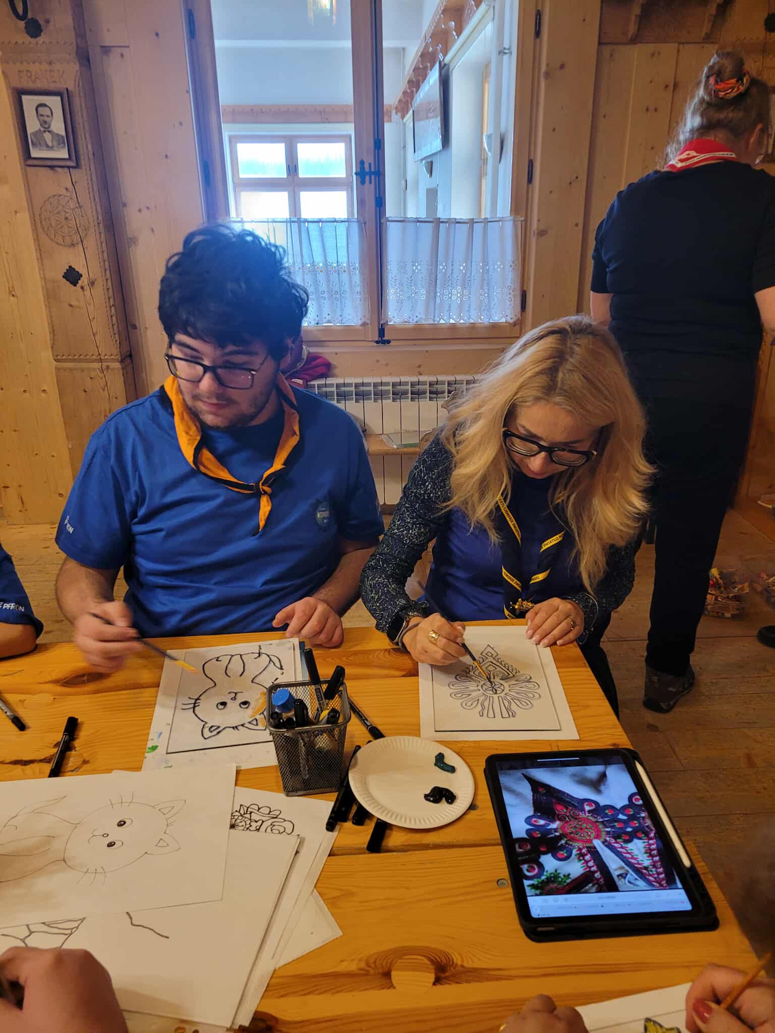 Na obrazku widać: dwie osoby, stół, kartki