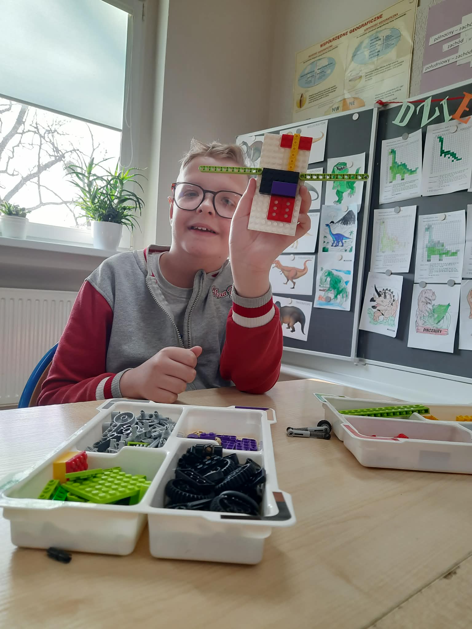 Na obrazku widać : osobę , stol, okno, klocki.