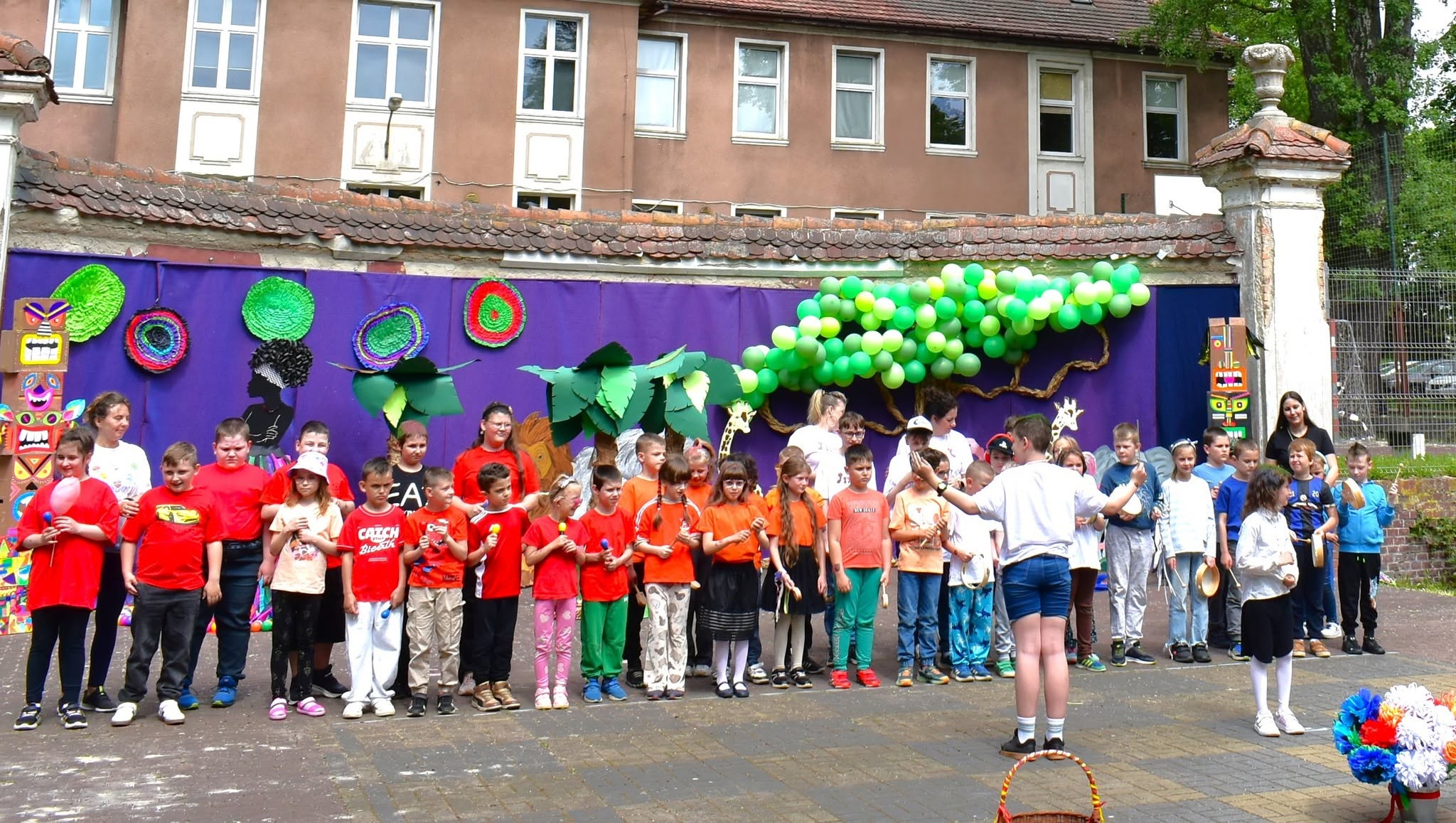 Na obrazku widać: grupę osób, makiety zwierzat, drzew, balony.