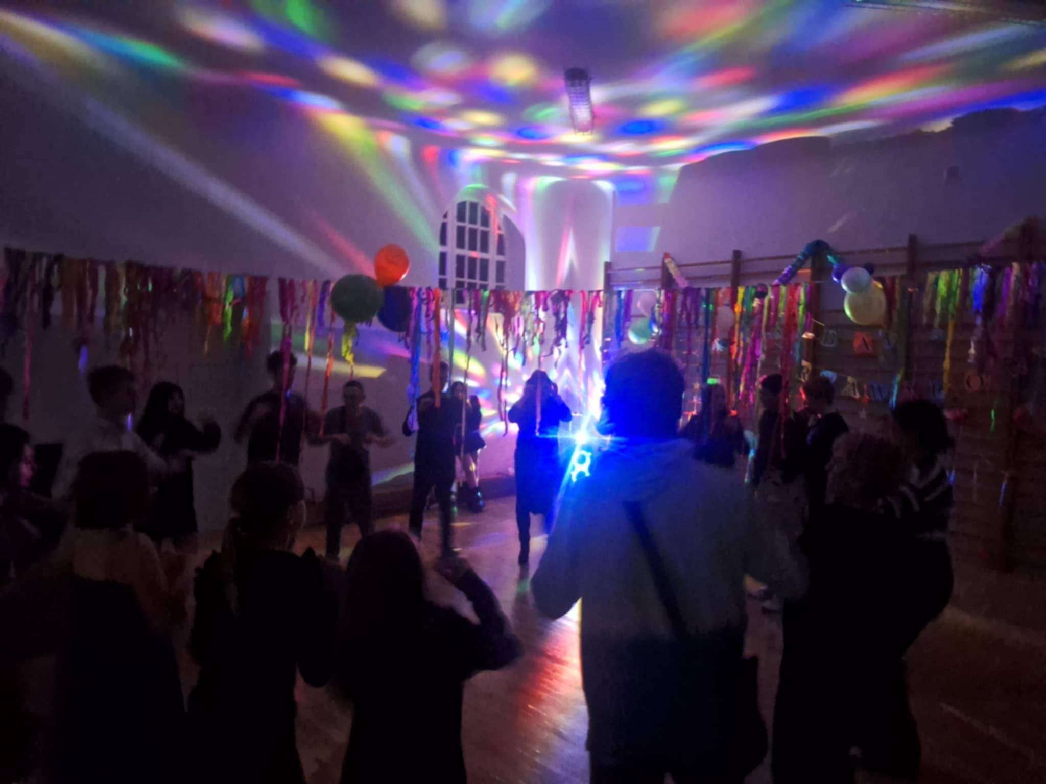 Na obrazku widać : grupę osób, kolorowe światła , sufit.