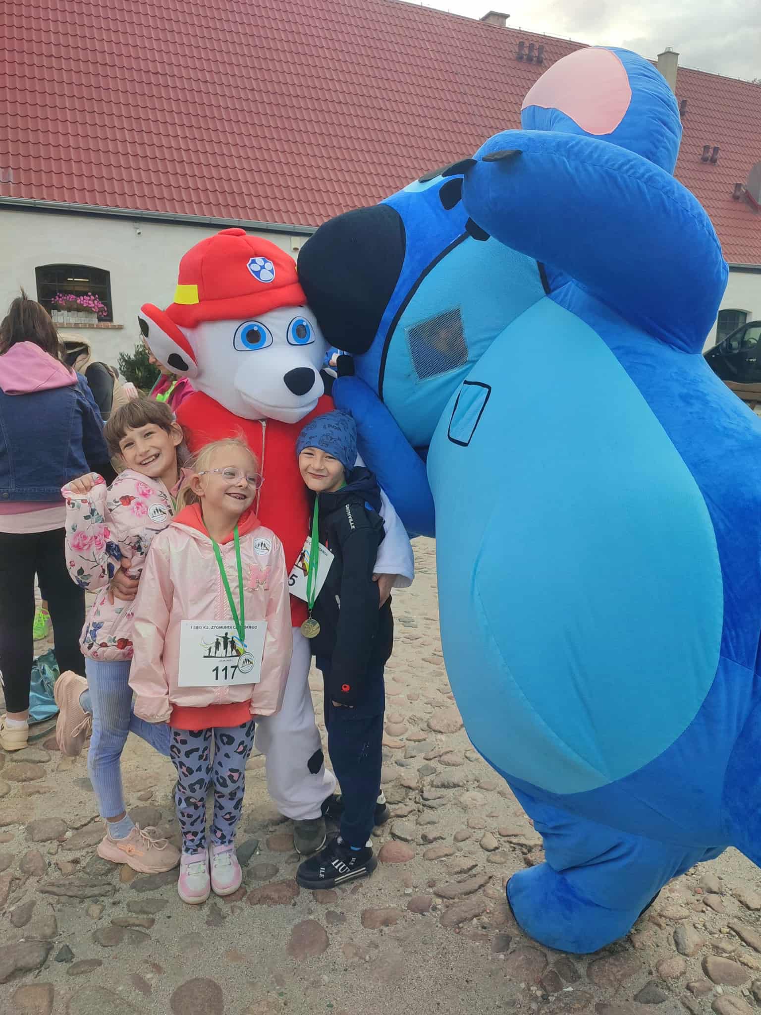 Na obrazku widać: grupę osób, 2 duże maskotki