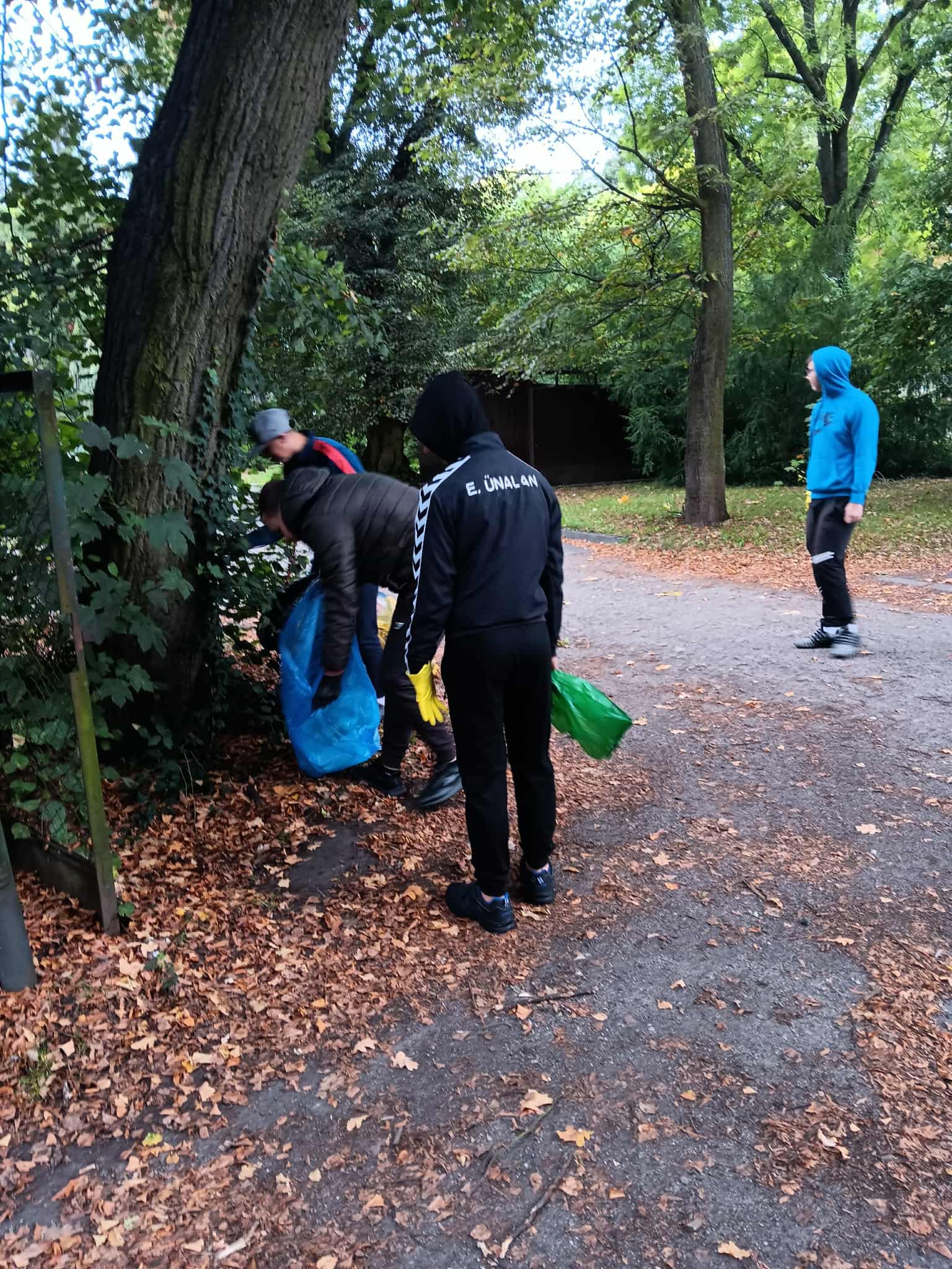 Na obrazku widać: grupę osób, worki, drzewa