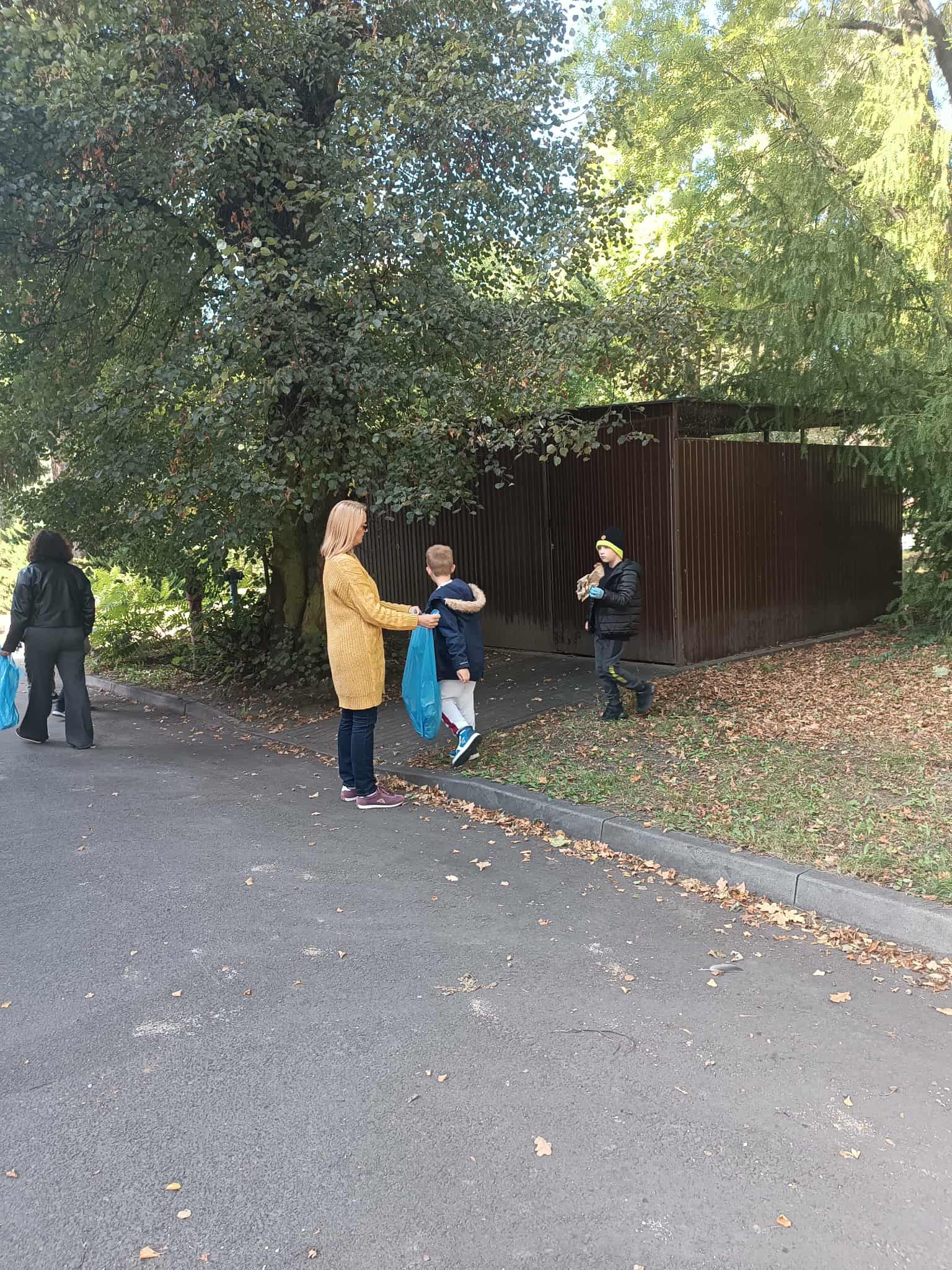 Na obrazku widać: grupę osób, drzewa, worki