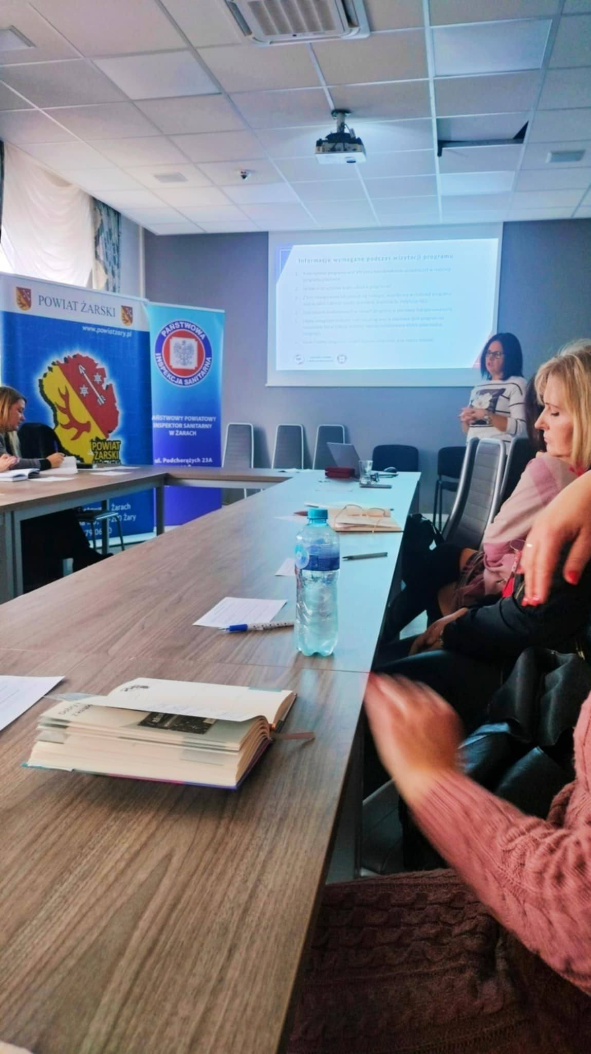 Na obrazku widać: grupę osób, blat stolu. ekran.