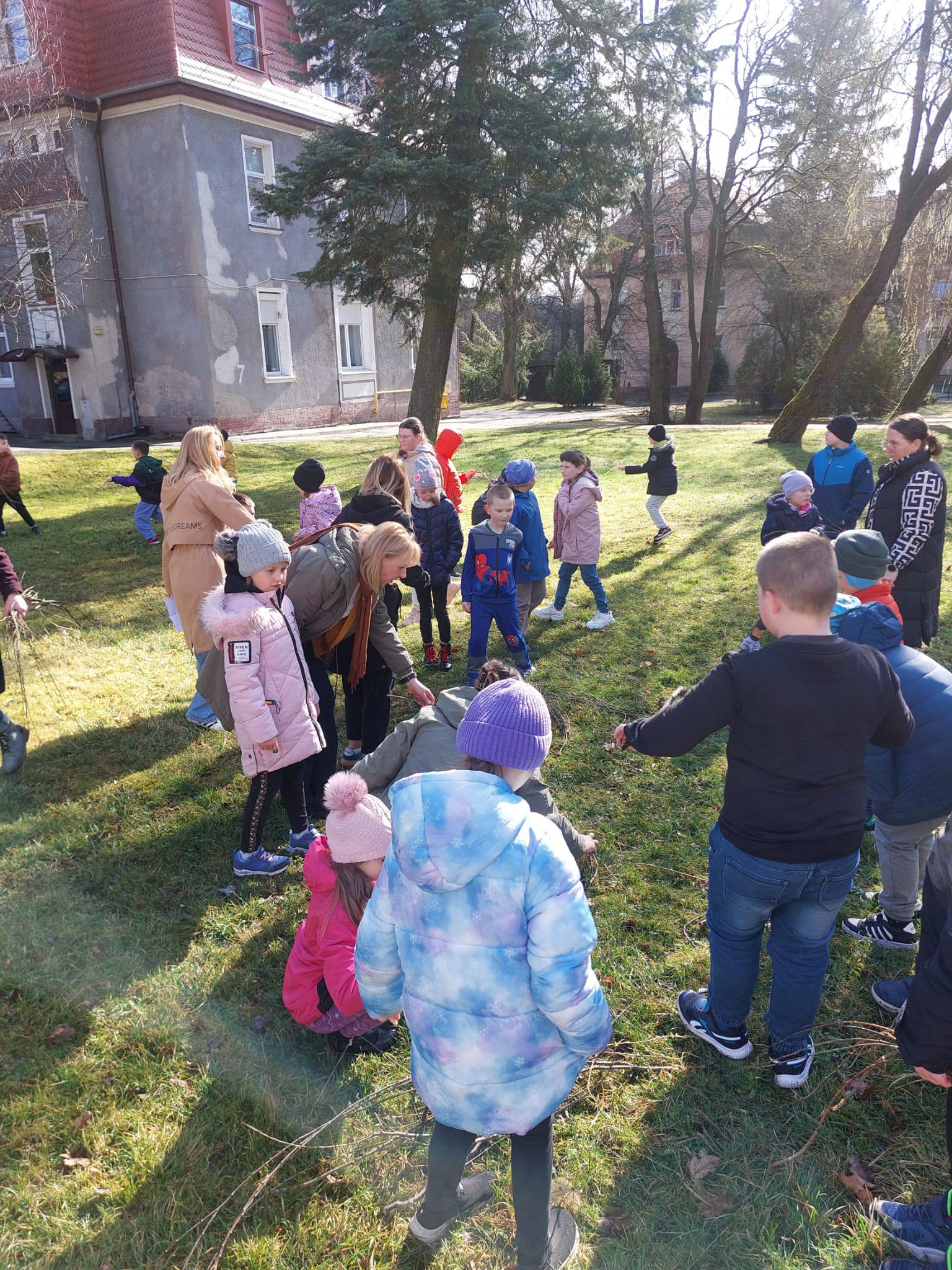 Na obrazku widać: osoby, drzewa, budynek