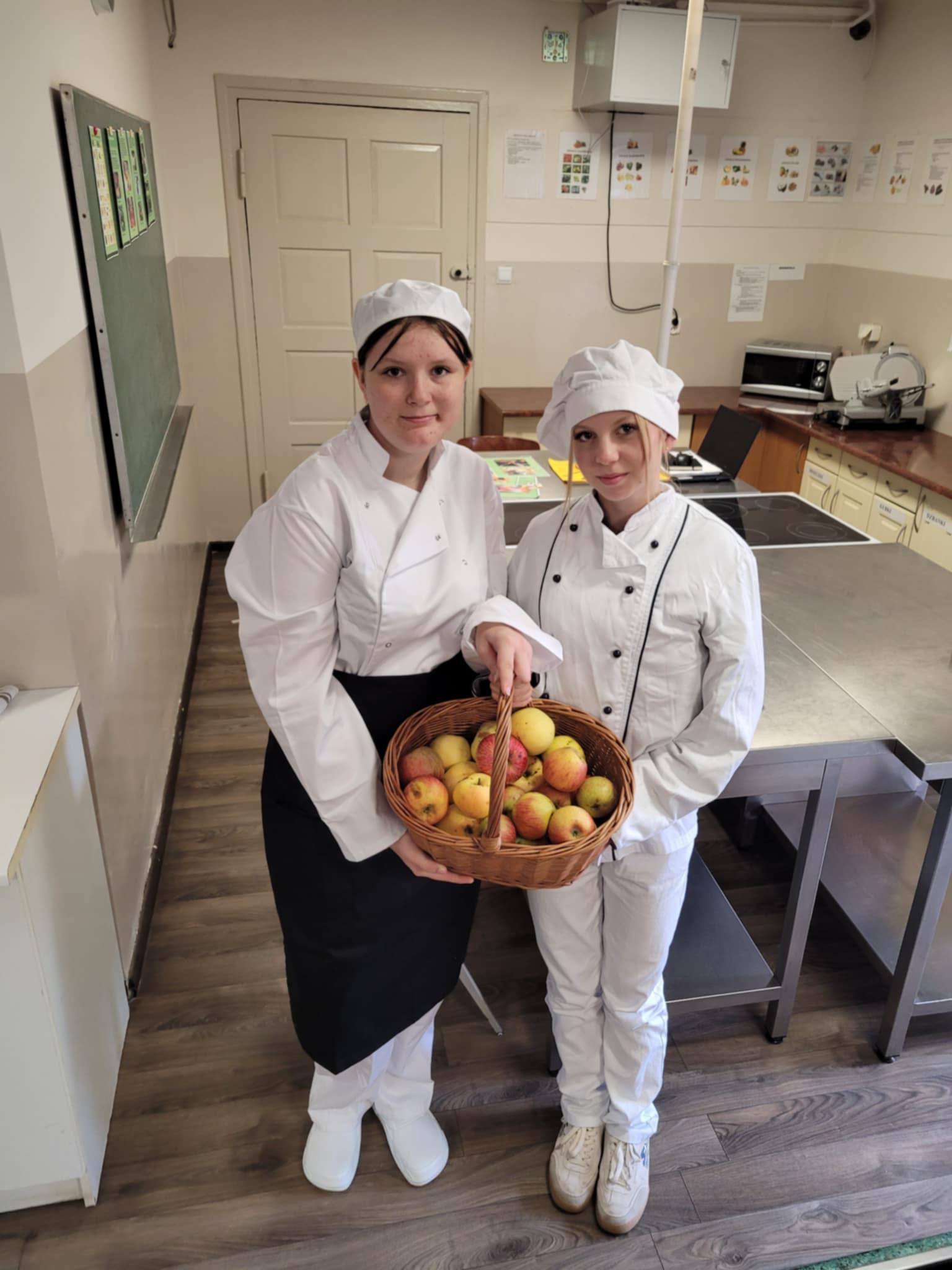 Na obrazku widać: dwie osoby, koszyk z jabłkami